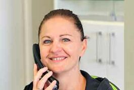 Frau lächelnd, hält Telefon am Ohr, braune Haare, Vereinskleidung mit grünem Akzent, freundlicher Ausdruck.