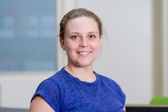 Person, lächelt, blauer Pullover, hellbraunes Haar, heller Hintergrund.